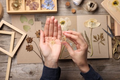 Photo of Woman putting dry flowers into notebook at wooden table, top view