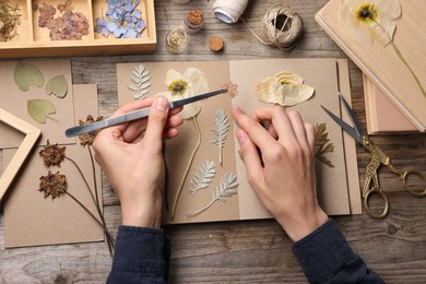 Photo of Woman putting dry flowers into notebook at wooden table, top view