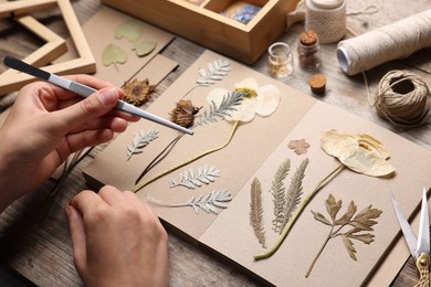 Photo of Woman putting dry flowers into notebook at wooden table, closeup