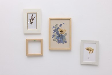 Photo of Beautiful dry flowers and leaves in picture frames on white wall