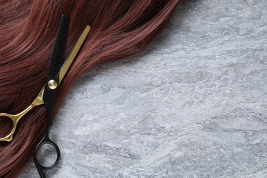 Photo of Auburn hair strand and hairdresser's scissors on grey background, closeup. Space for text
