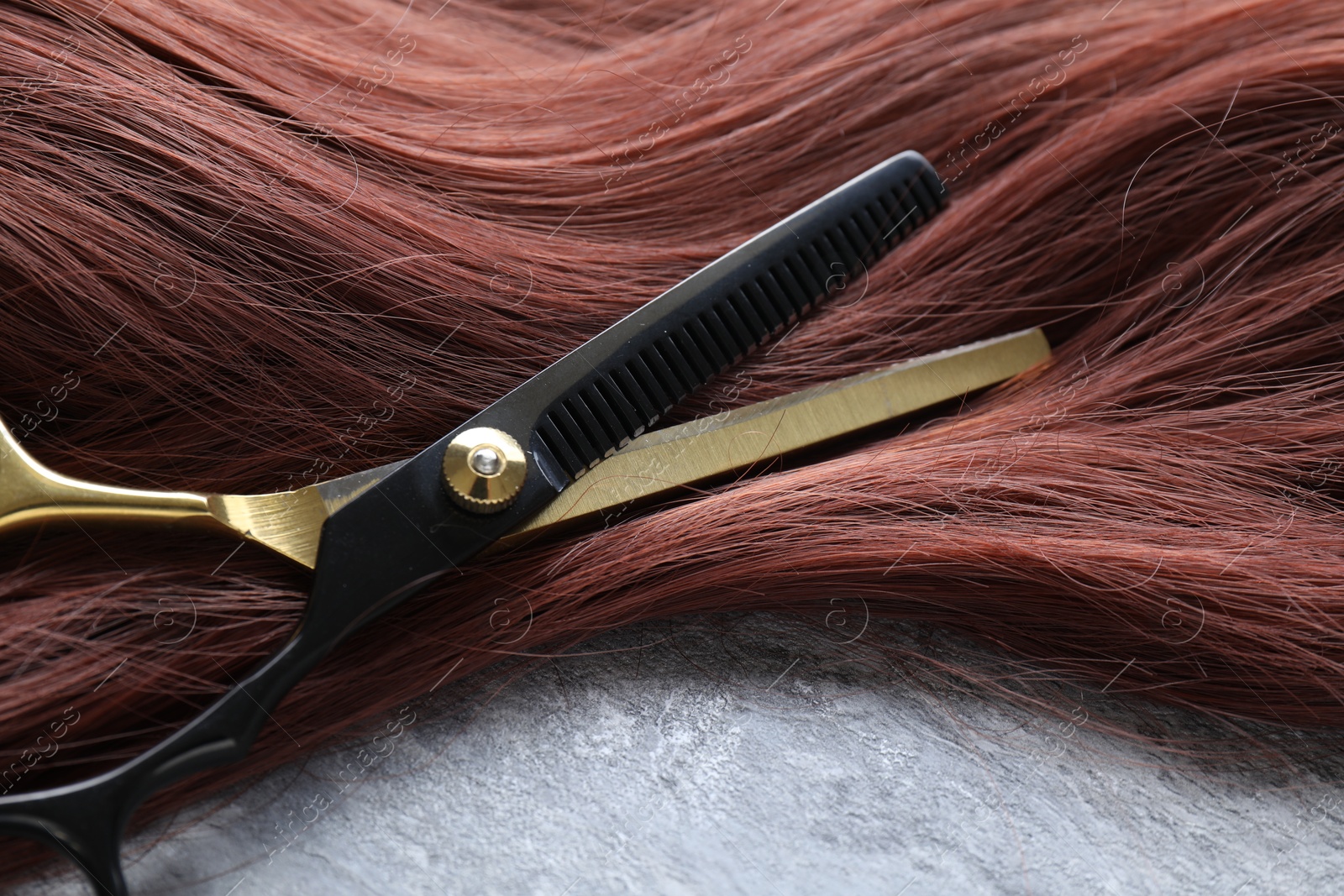 Auburn hair strand and hairdresser's scissors on grey background, closeup Photo of Auburn hair strand and hairdresser's scissors on grey background, closeup