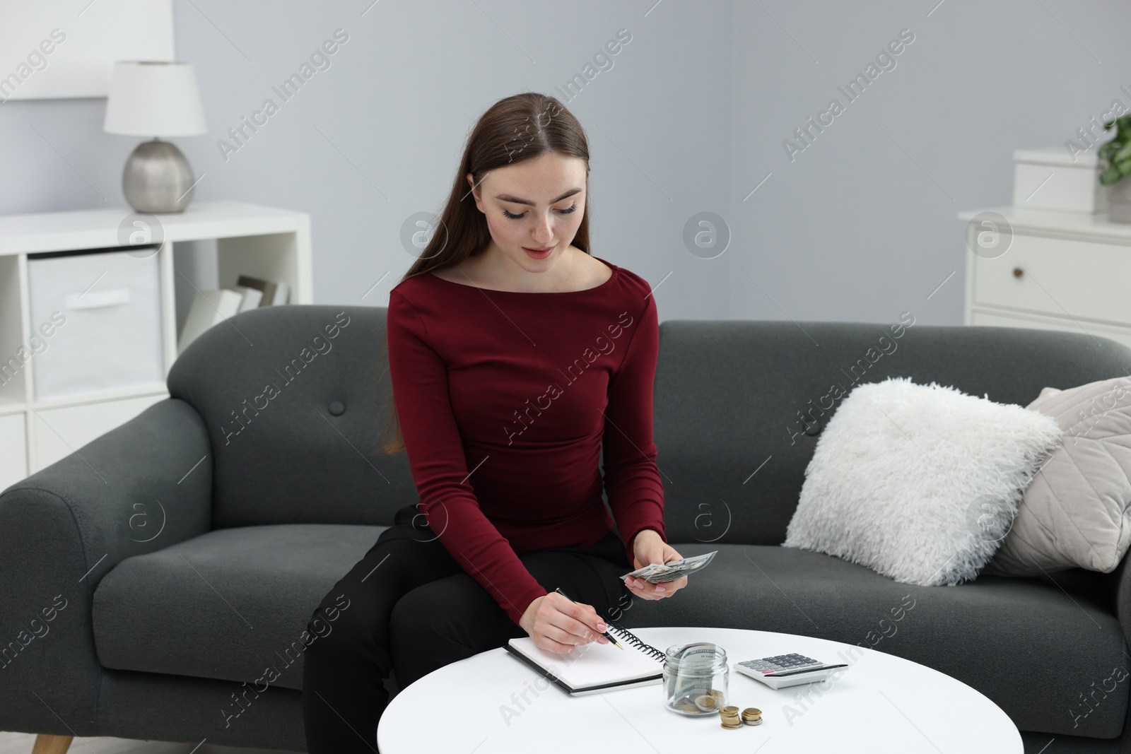 Woman counting dollar banknotes on sofa indoors Photo of Woman counting dollar banknotes on sofa indoors