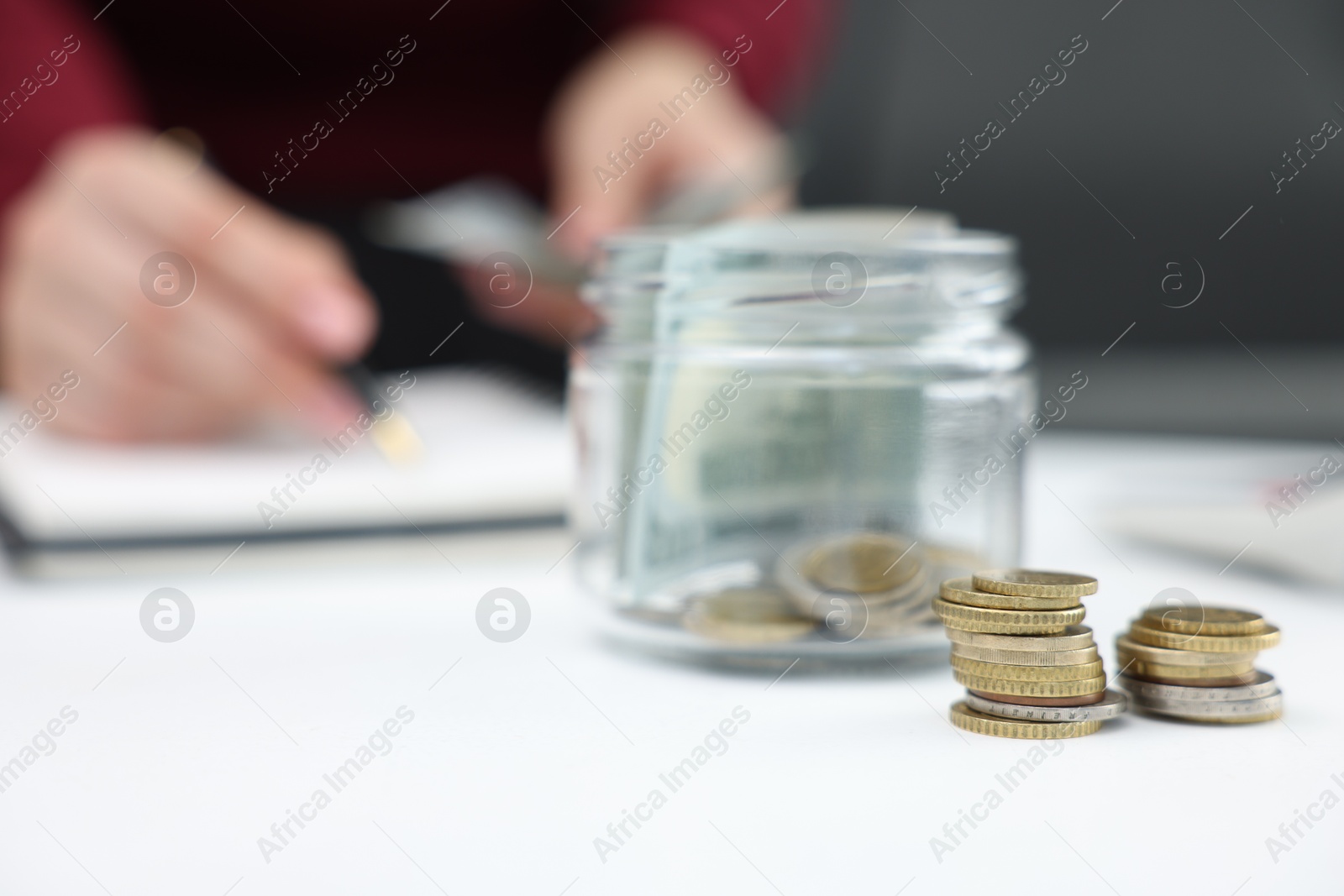 Photo of Woman counting dollars at table indoors, focus on glass jar with money