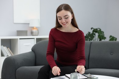 Photo of Woman putting coin into glass jar and using calculator indoors