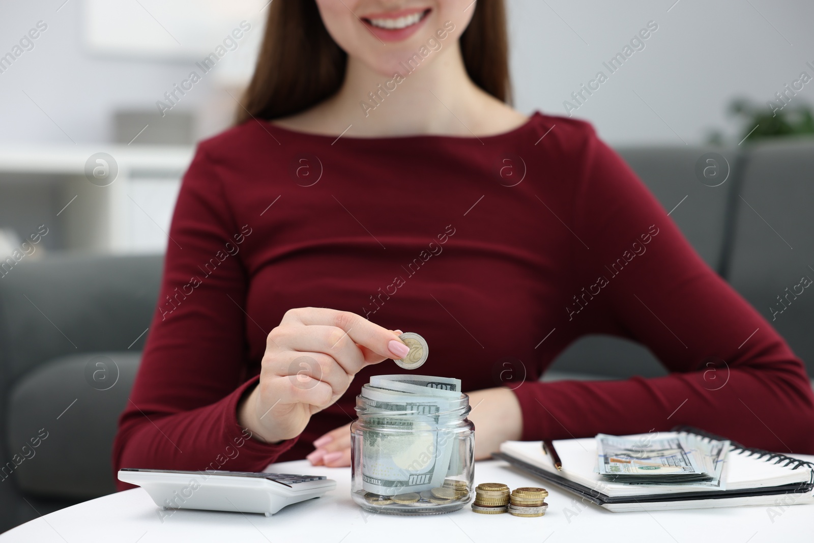 Photo of Woman putting coin into glass jar at table indoors, closeup