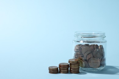 Photo of Glass jars with coins on light blue background, closeup. Space for text