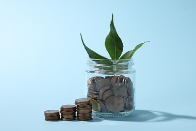 Photo of Glass jar with coins and sprout on light blue background, closeup