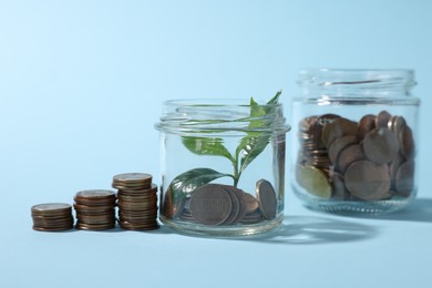 Photo of Glass jars with coins and sprout on light blue background, closeup
