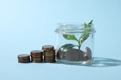Photo of Glass jar with coins and sprout on light blue background, closeup