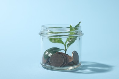 Photo of Glass jar with coins and sprout on light blue background, closeup
