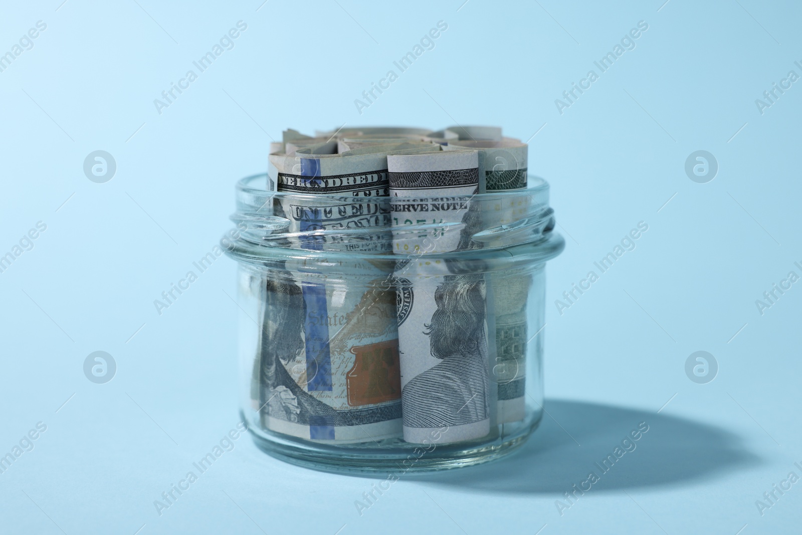 Photo of Glass jars with dollars on light blue background, closeup