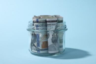 Photo of Glass jars with dollars on light blue background, closeup
