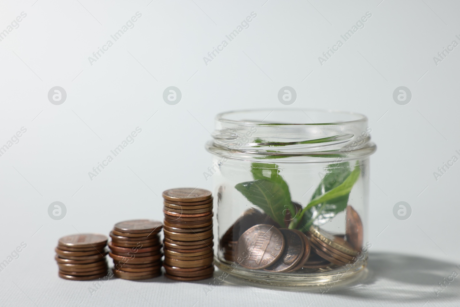 Photo of Glass jar with coins and sprout on light grey background, closeup