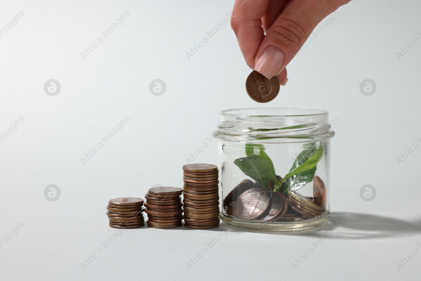 Photo of Woman putting coin into glass jar on light grey background, closeup