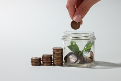 Photo of Woman putting coin into glass jar on light grey background, closeup