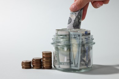 Photo of Woman putting dollar banknote into glass jar on light grey background, closeup