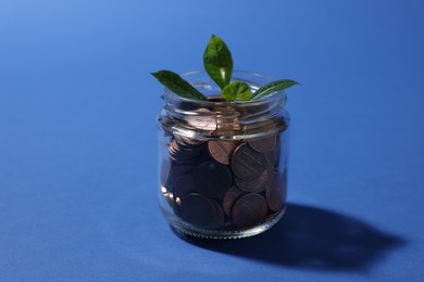Photo of Glass jar with coins and sprout on blue background, closeup