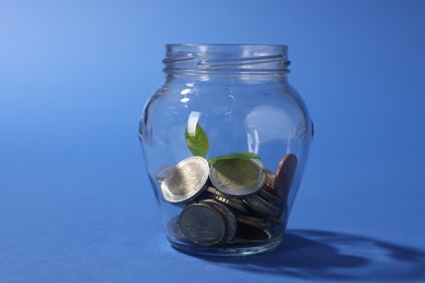 Photo of Glass jar with coins and sprout on blue background, closeup