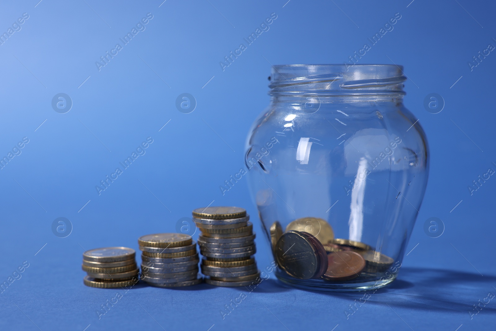 Photo of Glass jar with coins on blue background, closeup