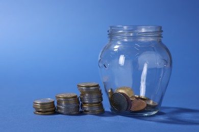 Photo of Glass jar with coins on blue background, closeup
