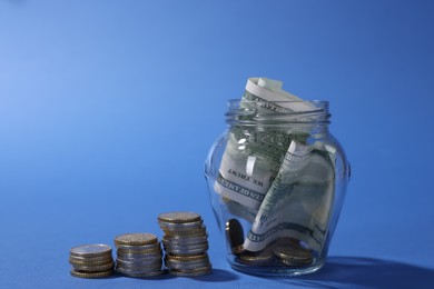 Photo of Glass jar with dollars and coins on blue background, closeup