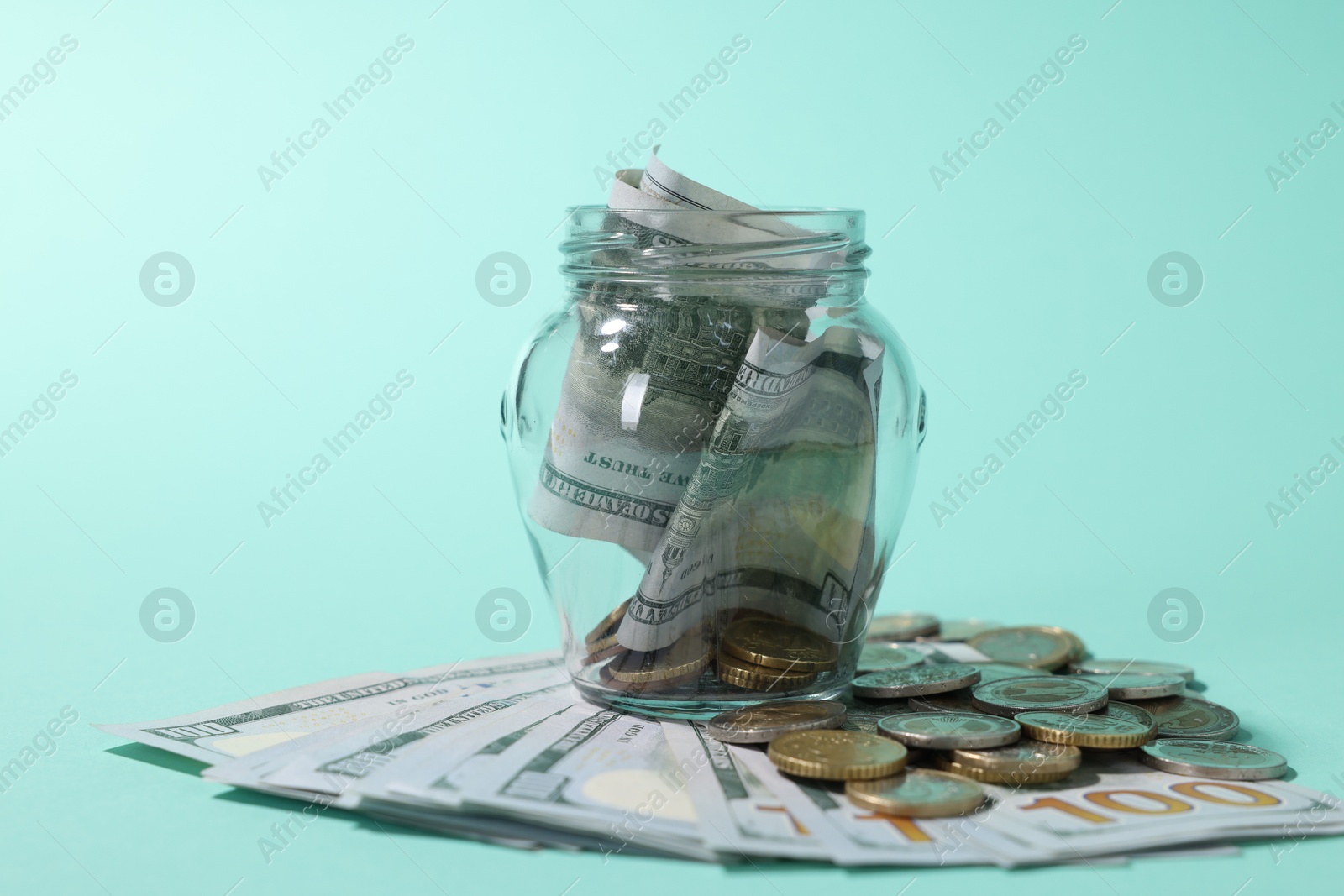 Photo of Glass jar with dollars and coins on light blue background, closeup