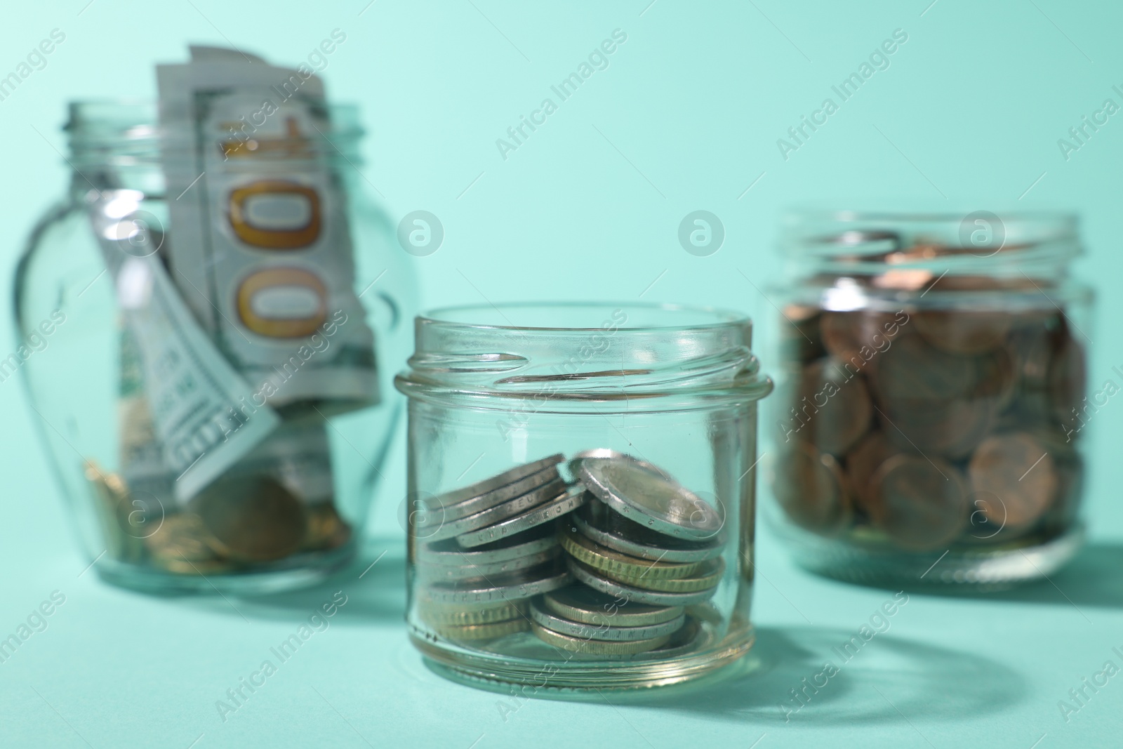 Photo of Glass jars with coins, sprout and dollars on light blue background, closeup