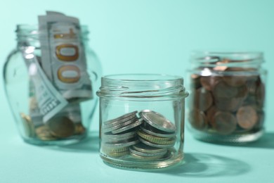 Photo of Glass jars with coins, sprout and dollars on light blue background, closeup