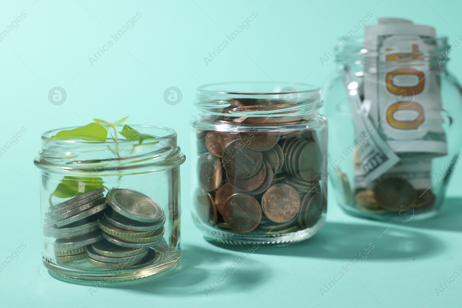 Photo of Glass jars with coins, sprout and dollars on light blue background, closeup