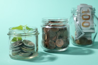Photo of Glass jars with coins, sprout and dollars on light blue background, closeup