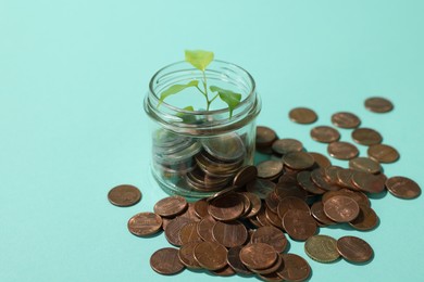 Photo of Glass jar with coins and sprout on light blue background, closeup