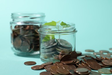 Photo of Glass jars with coins and sprout on light blue background, closeup