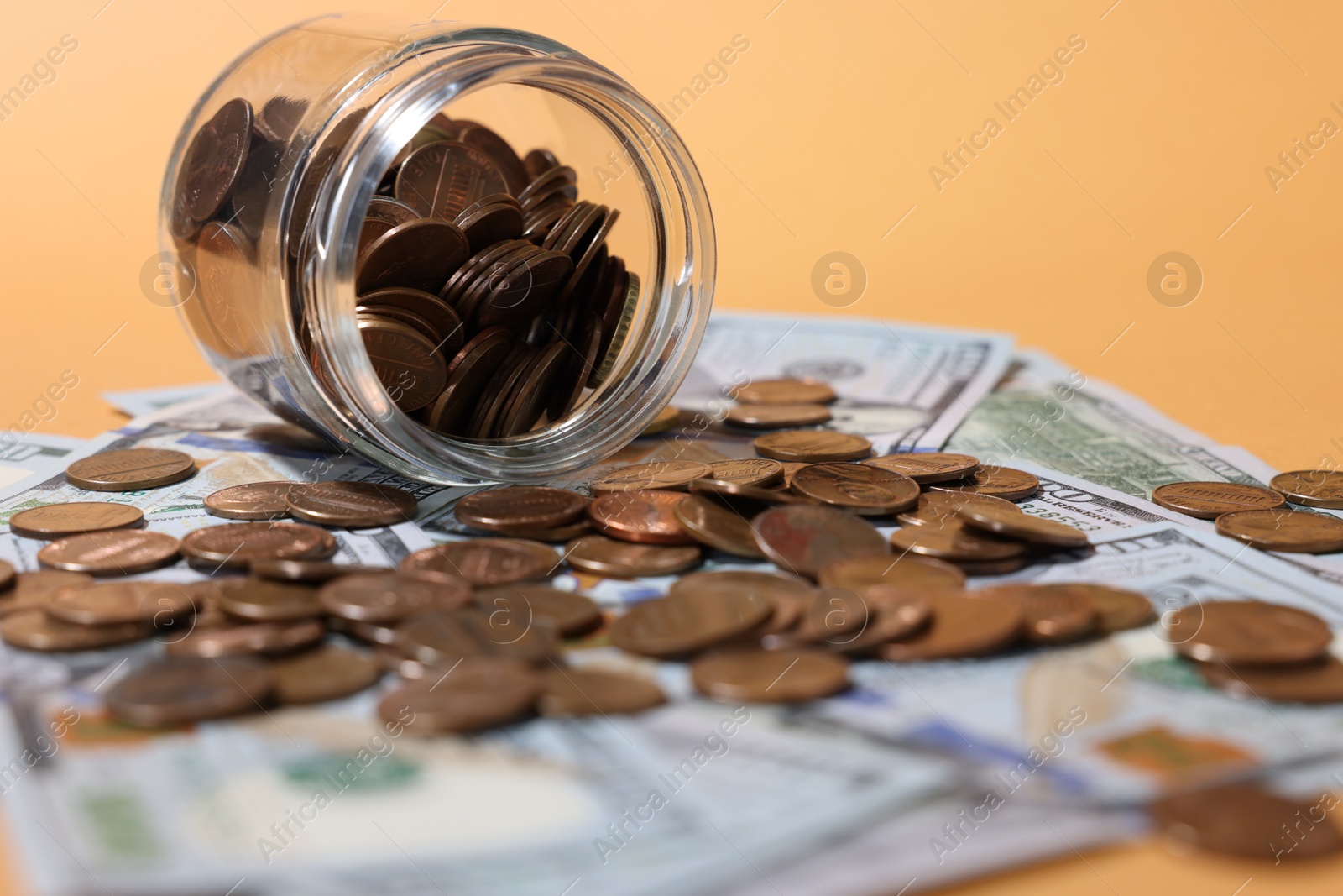 Photo of Glass jar with coins and dollars on pale orange background, closeup