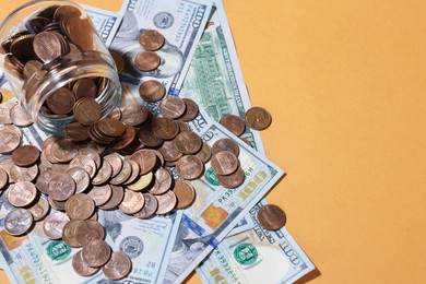 Photo of Glass jar with coins and dollars on pale orange background, above view. Space for text