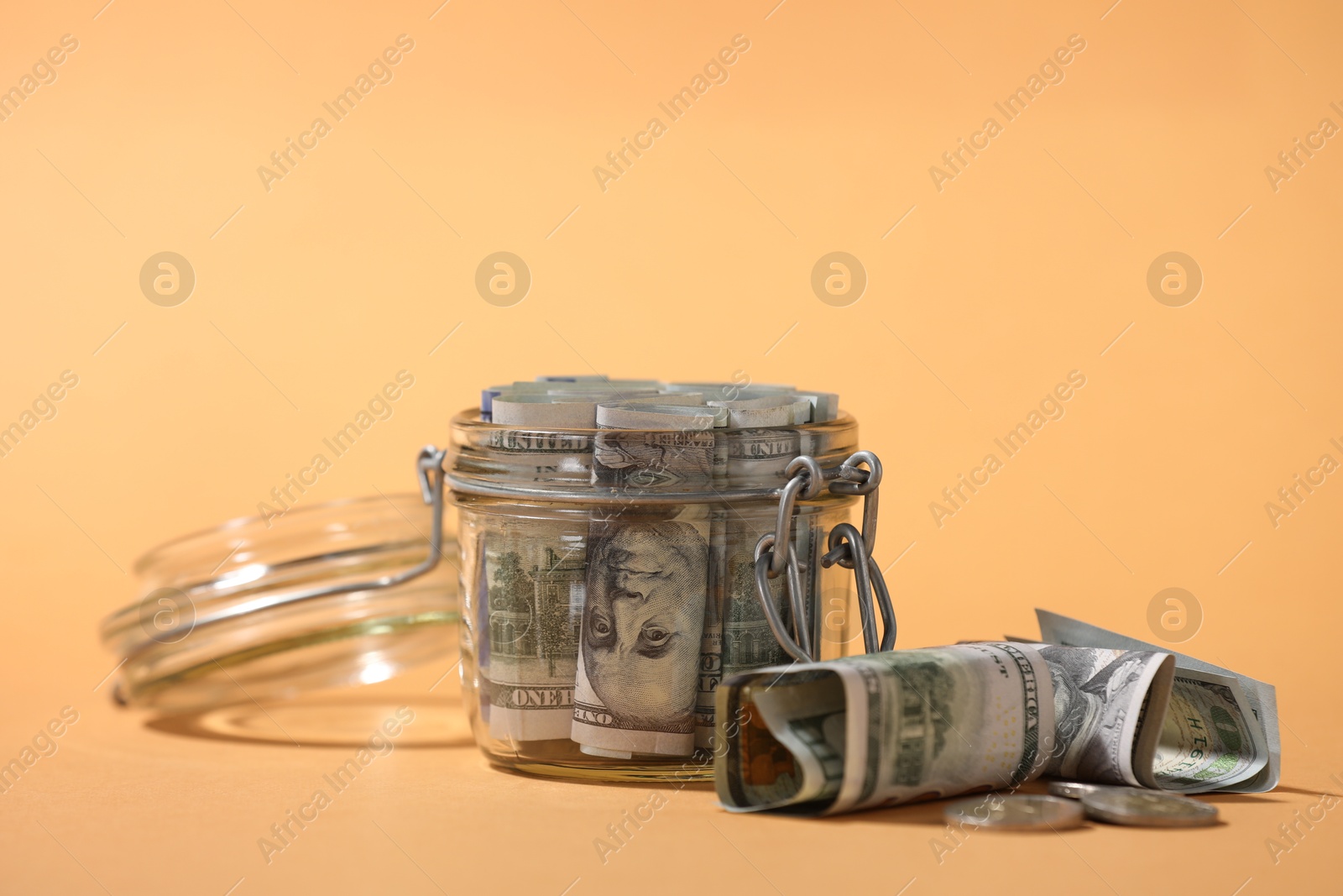 Photo of Glass jar with dollars and coins on pale orange background, closeup