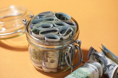 Photo of Glass jar with dollars on pale orange background, closeup