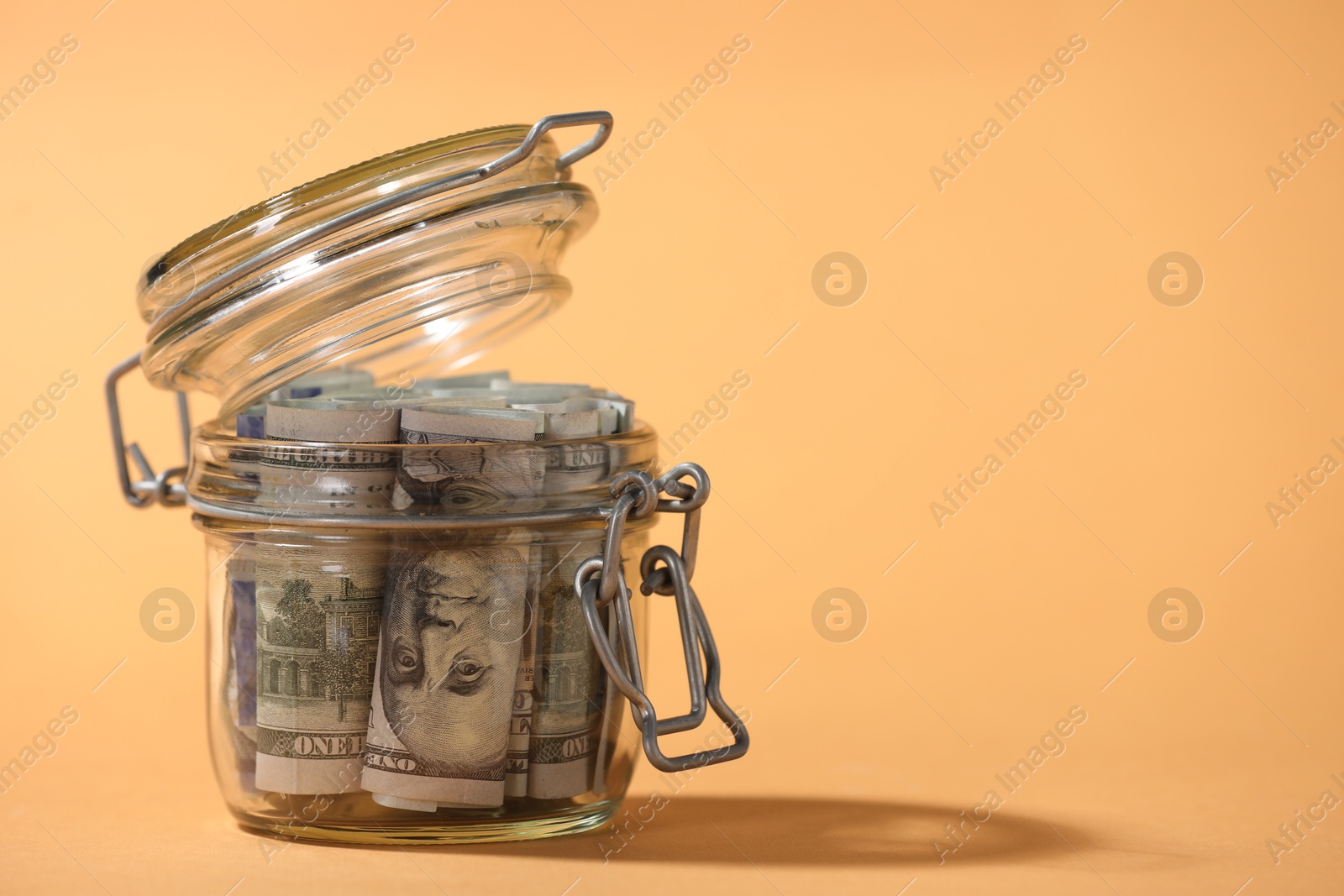 Photo of Glass jar with dollars on pale orange background, closeup. Space for text