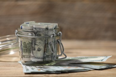 Photo of Glass jar with dollars on wooden table, closeup
