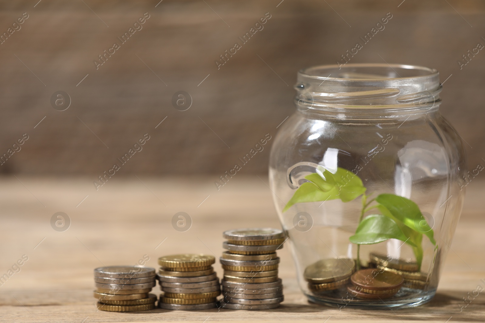 Photo of Glass jar with coins and sprout on wooden table, closeup. Space for text