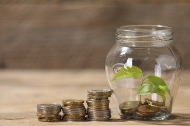 Photo of Glass jar with coins and sprout on wooden table, closeup. Space for text