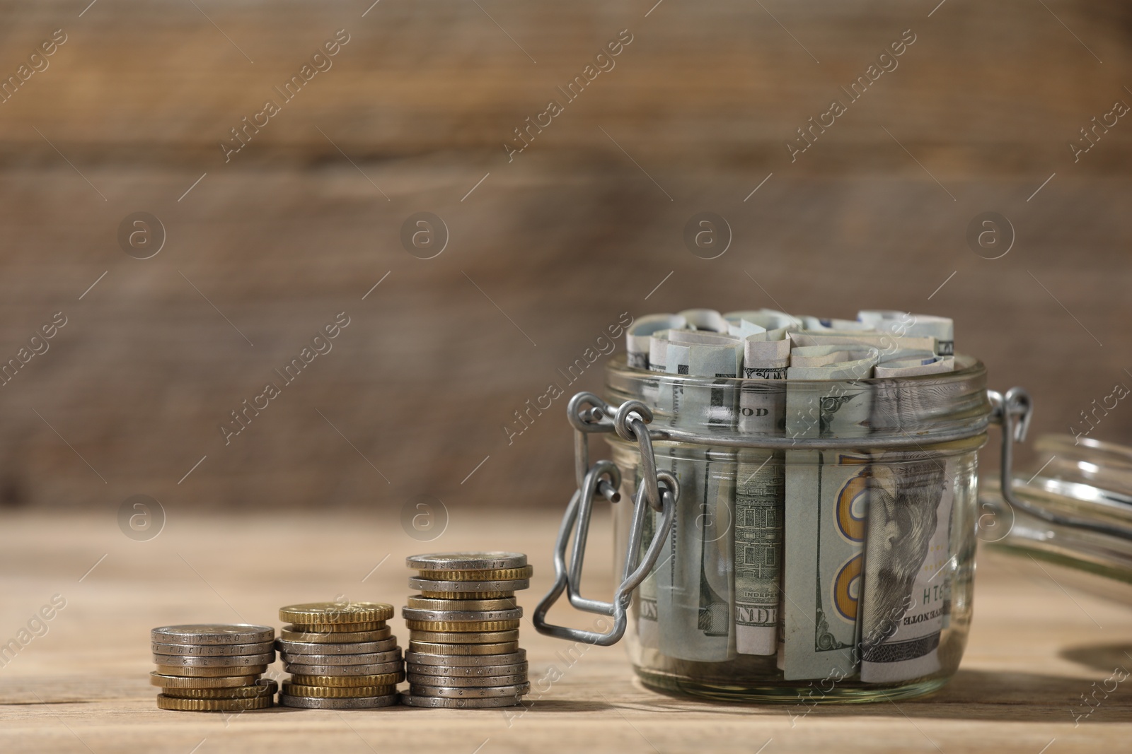 Photo of Glass jar with dollars and coins on wooden table, closeup