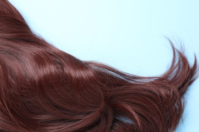 Photo of Lock of brown hair on light blue background, closeup. Space for text