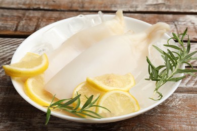 Photo of Pieces of raw squids with ice cubes, rosemary and lemon on color wooden table, closeup