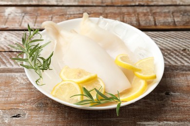Photo of Pieces of raw squids with ice cubes, rosemary and lemon on color wooden table, closeup