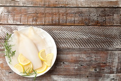 Photo of Pieces of raw squids with ice cubes, rosemary and lemon on color wooden table, top view. Space for text