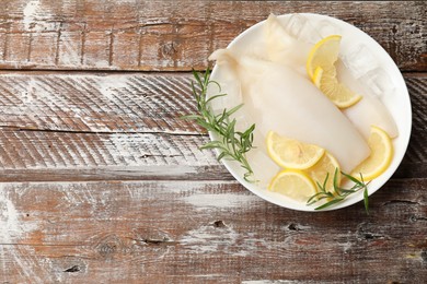 Photo of Pieces of raw squids with ice cubes, rosemary and lemon on color wooden table, top view. Space for text