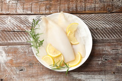Photo of Pieces of raw squids with ice cubes, rosemary and lemon on color wooden table, top view