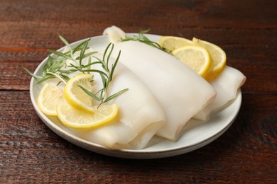 Photo of Pieces of raw squids with rosemary and lemon on wooden table, closeup