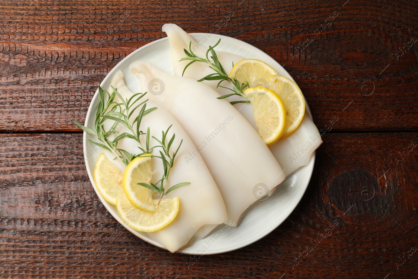 Photo of Pieces of raw squids with rosemary and lemon on wooden table, top view